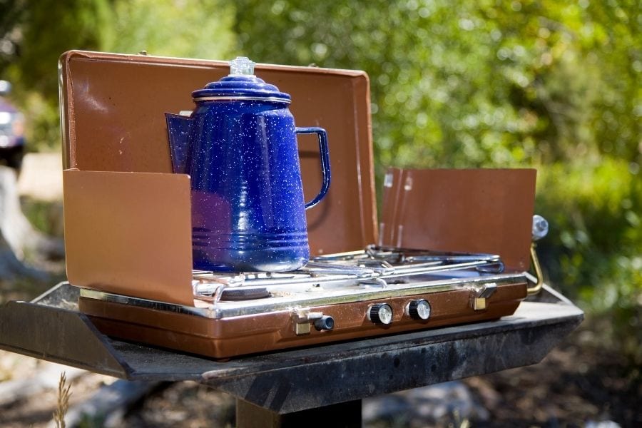 一个蓝色的热水水壶放在一个黄铜色的野营炉上